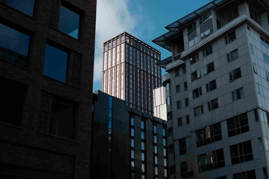 這張圖片展示了城市中現代化的建築群，有高樓大廈，也有設計感獨特的建築，整體給人一種都市、專業、甚至略帶競爭或高壓的氛圍。天空背景也顯得有些陰沉或嚴肅。